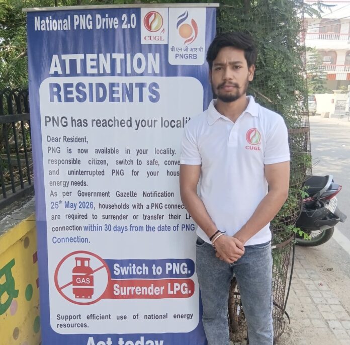 रामपुर गार्डन क्षेत्र में घरेलू पीएनजी कनेक्शन के प्रचार अभियान के दौरान जागरूकता पोस्टर के साथ खड़ा सीयूजीएल का प्रतिनिधि। …