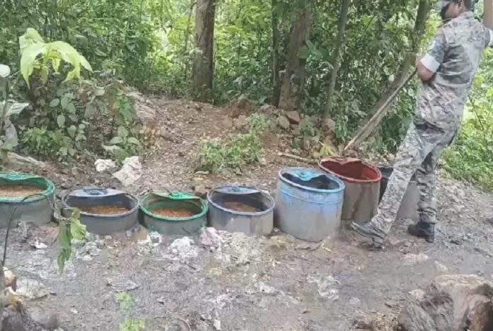 पुलिसकर्मी अवैध शराब भट्टी को ध्वस्त करते हुए